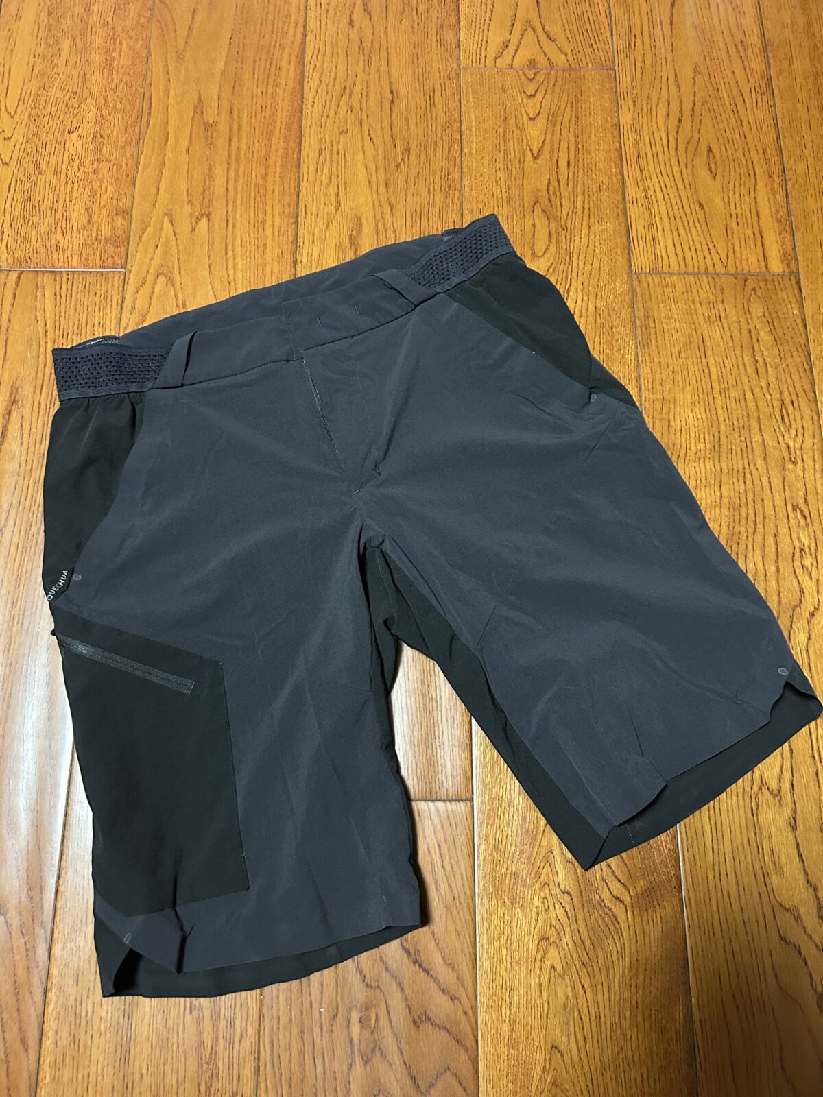 黑色迪卡侬 MH500 徒步短裤平铺实拍，可见主体面料与局部耐磨贴片的拼接。